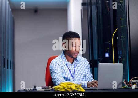 Smiling african american male computer technician using laptop working in business server room Stock Photo