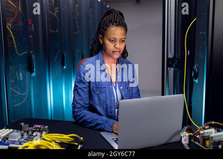 African american female computer technician using laptop working in server room Stock Photo