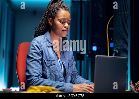 African american female computer technician using laptop working in server room Stock Photo