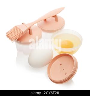 Set of heat resistant silicone molds for poached egg, basting brush and fresh raw eggs isolated on white background. Utensil for cooking. Poached egg. Stock Photo