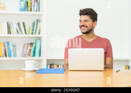 Laughing hispanic mature man with beard at computer indoors at home Stock Photo