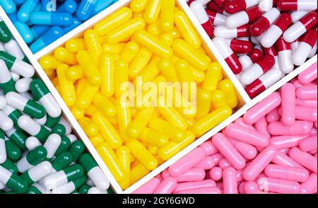 Top view colorful capsule pills in a plastic tray. Yellow, pink, red, green, and blue capsule pills. Antibiotics, vitamins, and supplements capsules. Stock Photo