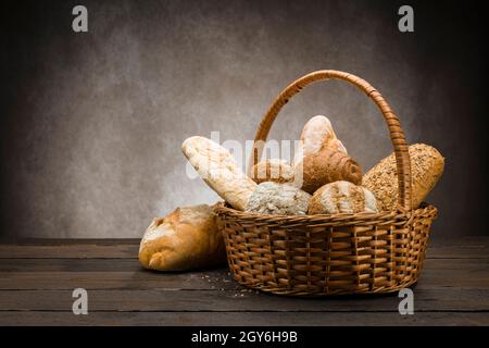 assortment of baked bread in wicker basket on wooden table Stock Photo