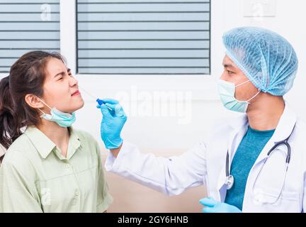 Coronavirus test, Doctor man take saliva sample through nose with cotton swab to check coronavirus test from Asian young woman, Covid-19 pandemic outb Stock Photo