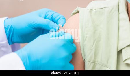 Vaccination, Doctor man after injection coronavirus vaccine to young woman shoulder he rubber protective gloves putting an adhesive bandage plaster, C Stock Photo