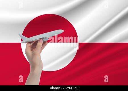 Airplane in hand with national flag of Greenland. Travel to Greenland.