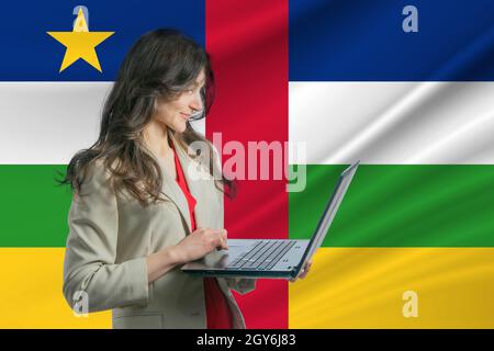 Freelance in Central African Republic. Beautiful young woman freelancer uses laptop computer against the background of the flag of Central African Rep Stock Photo