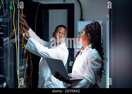 African american computer technicians using laptop working in server room Stock Photo