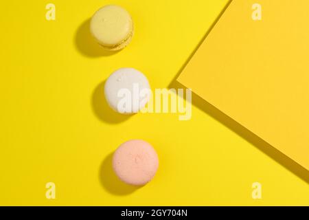 round multicolored macarons on a yellow background with a shadow on a yellow background. Gourmet almond flour dessert, top view Stock Photo