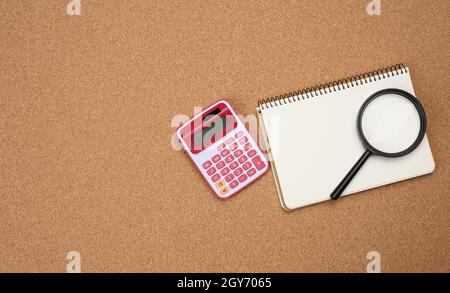 pink calculator, notebook with blank white sheets and black magnifier on a brown background. Banner for business, top view Stock Photo