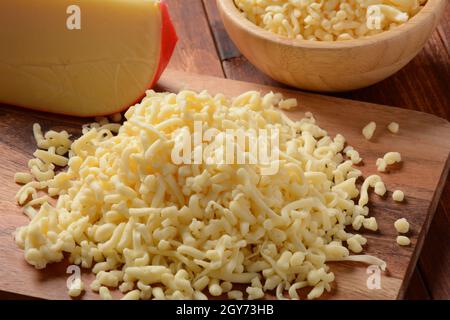 Heap of shredded cheese on small wooden board. Grated cheese for cooking on a cutting board on a wooden background Stock Photo