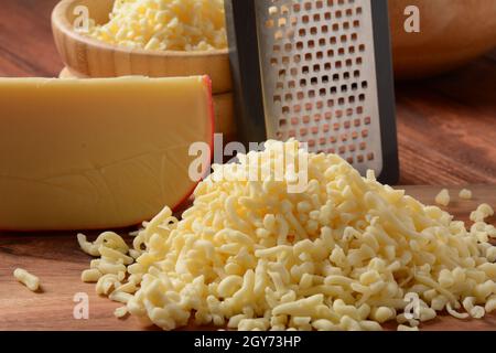 Heap of shredded cheese on small wooden board. Grated cheese for cooking on a cutting board on a wooden background Stock Photo