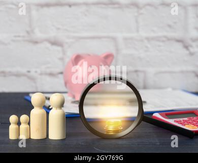 wooden family figurines and  pink ceramic piggy bank on blue background. Concept of accumulating cash for buying a house and a car, money in the bank Stock Photo