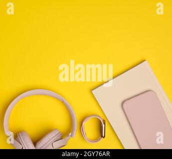 pink wireless headphones, smartphone and smart watch on a yellow background. Things and gadgets for a modern person, top view Stock Photo