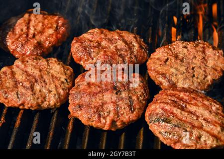 Close up searing and smoking beef or pork meat barbecue burgers for hamburger on bbq fire flame grill with cast iron metal grate, high angle view Stock Photo