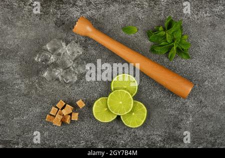 Close up mojito cocktail ingredients set flat lay, wooden muddler, brown sugar, heap of fresh green mint leaves, lime slices and ice cubes on table, e Stock Photo