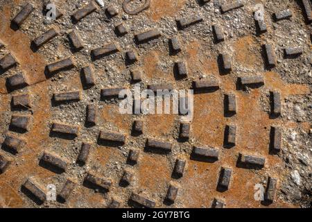 Rusty sewer manhole cover. Geometric pattern on the cover of the sewer manhole. Close-up view of the texture of the old rusty metal sewer manhole. Stock Photo