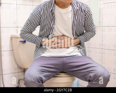 Young man holding his abdomen feels sick and constipation in the toilet Stock Photo