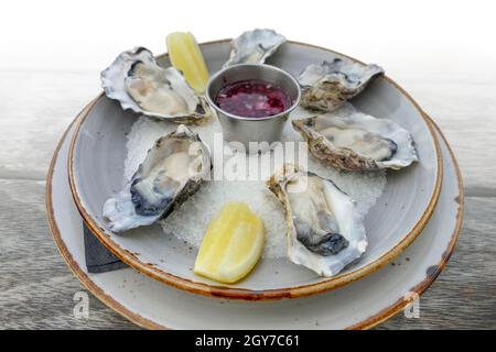 plate with fresh opened oysters and dip on a wooden table, gradient isolated in white back Stock Photo