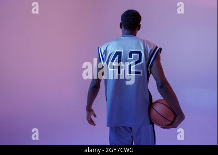 Basketball player poses with ball in studio, back view. Professional male baller in sportswear playing sport game, tall sportsman Stock Photo