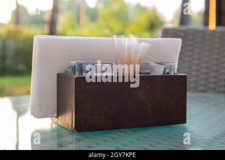 A brown wooden napkin holder and toothpicks sit on the glass table of the cafe, illuminated by the sun's rays. Table setting in the restaurant. Glass Stock Photo