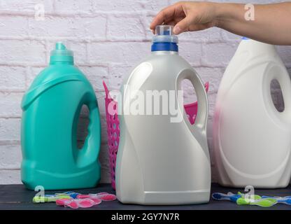 woman's hand holding a large white plastic bottle with detergent for washing clothes against a white brick wall background Stock Photo