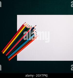 A blank white sheet and colored pencils for drawing on a plain textured background with space for copying and lettering. Layout, mockup free space. Stock Photo