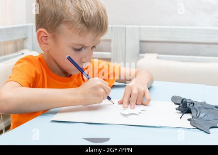 A boy draws and cuts a Halloween decoration at home from black paper. DIY craft decorations. Child makes black bats out of paper, origami Stock Photo