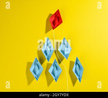 group of blue paper boats and one red led on a yellow background. Strong leader concept, growth of unique and talented employees, top view Stock Photo