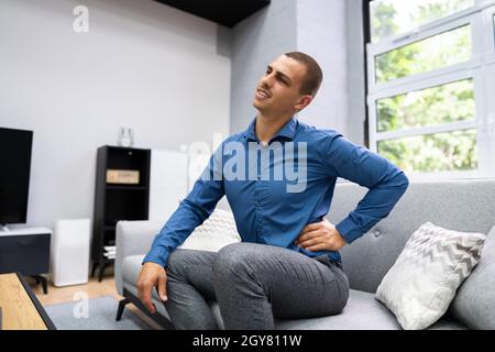 Man Sitting On Sofa Having Back Pain Stock Photo