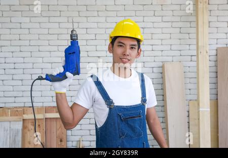 Asian carpenter wearing a yellow hardhat, poses confidently before beginning the job of receiving orders at the wood working place. Morning work atmos Stock Photo