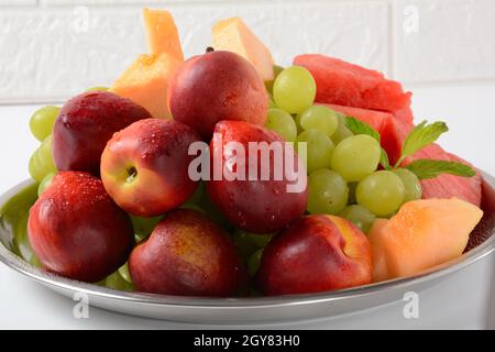 Fruit mix. Nectarine, grapes,  watermelon, melon. Pieces of fruit on a plate lie on a silver tray on white background. Stock Photo