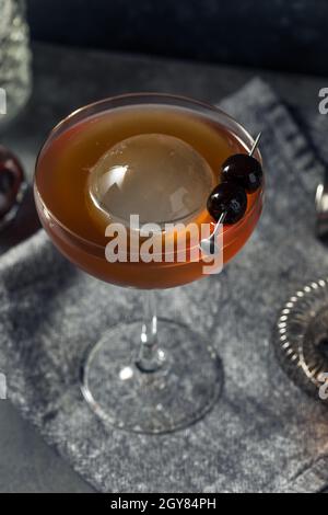 Boozy Cold Manhattan Cocktail with a Big Ice Cube and Cherries Stock Photo
