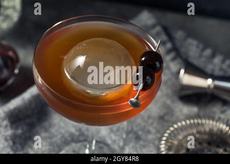 Boozy Cold Manhattan Cocktail with a Big Ice Cube and Cherries Stock Photo
