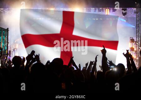 Soccer fans supporting England - crowd celebrating in stadium with raised hands against England flag Stock Photo