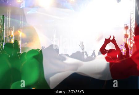 Soccer fans supporting Italy - crowd celebrating in stadium with raised hands against italian flag Stock Photo