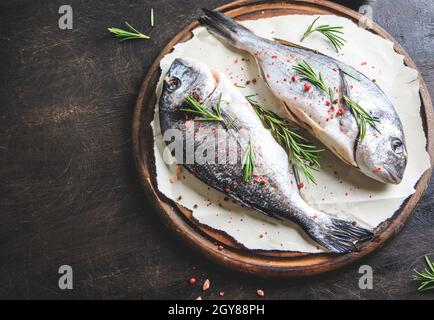 fresh raw dorado fish on a cutting wood board with pink himalayan salt, pink peppercorns and rosemary Stock Photo