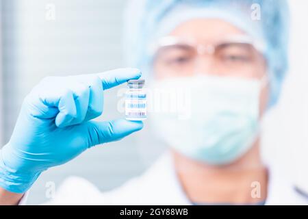 Young doctor or scientist in uniform wearing a face mask showing up coronavirus vaccine, nurse man holding bottle COVID-19 vaccination at laboratory,