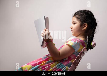 Little girl reading a book with blank cover in front of body, editable mock-up series template ready for your design, book cover selection path includ Stock Photo