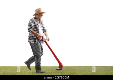 Full length shot of a mature man walking and trimming grass with a trimming machine isolated on white background Stock Photo