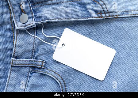Blank white cardboard tag or label with rope on jeans clothes background Stock Photo