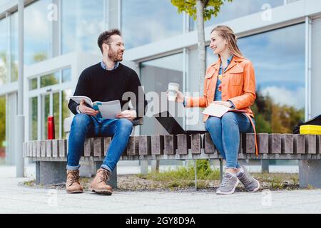 Man and woman student chatting on university campus in front of main building Stock Photo