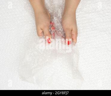 female hand holding crumpled piece of polyethylene with air bubbles on a white background, packing material, top view Stock Photo