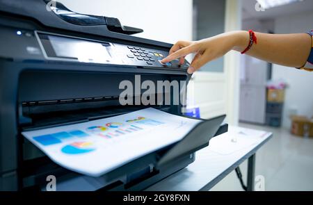 Office worker prints paper on multifunction laser printer. Copy, print, scan, and fax machine in office. Document and paper work. Print technology. Ha Stock Photo