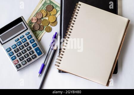 Plain Spiral Notebook With Pen Beside Calculator And Coins On Table. Stock Photo