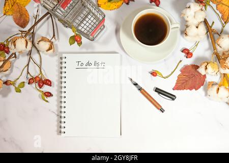 Notebook page wit text To Do List, coffee cup, shopping card and natural autumn decoration on a light marble background, seasonal holiday concept, cop Stock Photo