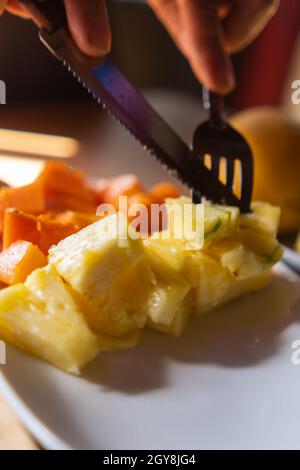 Hands cutting sliced fruit with fork and knife on plate Stock Photo
