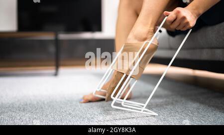Woman putting on compression stocking in living room, closeup