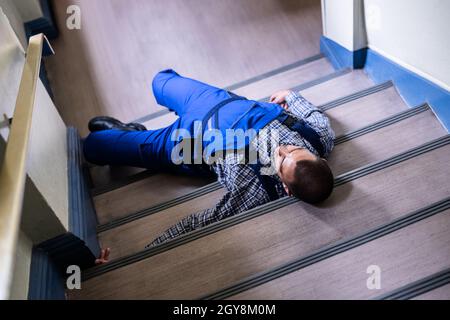 Worker Man Lying On Staircase After Slip And Fall Accident Stock Photo