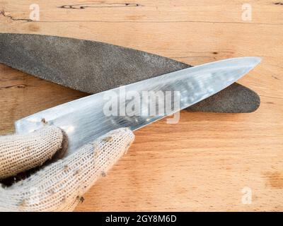 gloved hand sharpens kitchen knife closeup on whetstone Stock Photo